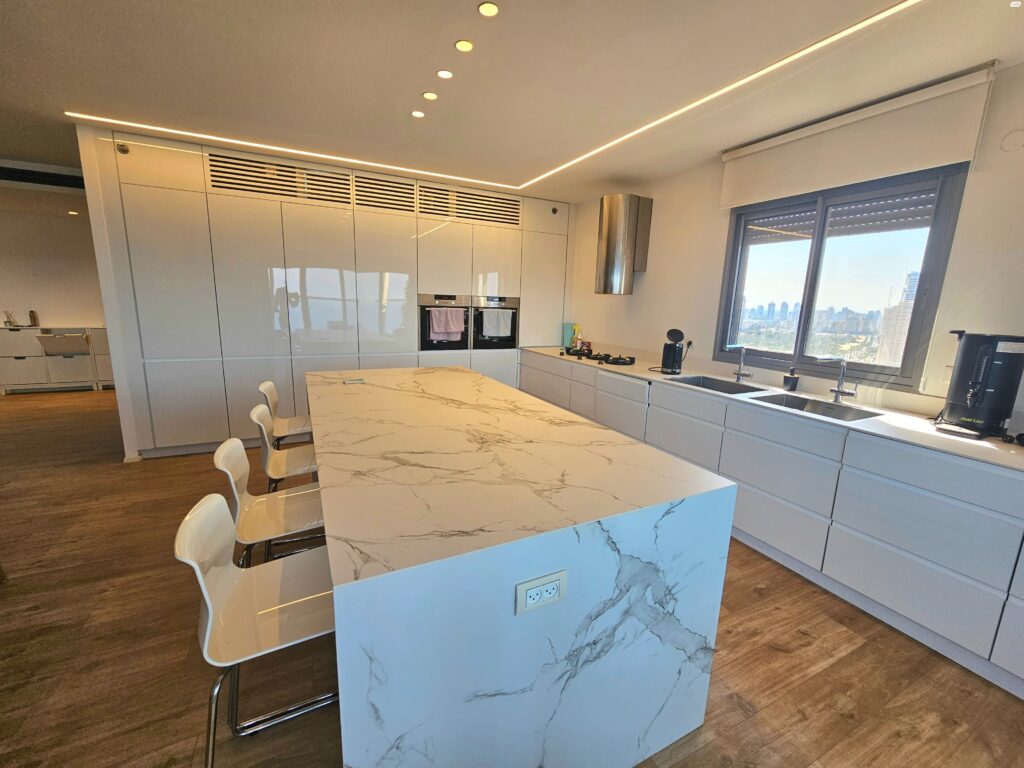 Modern white kitchen with large marble island and sea view window